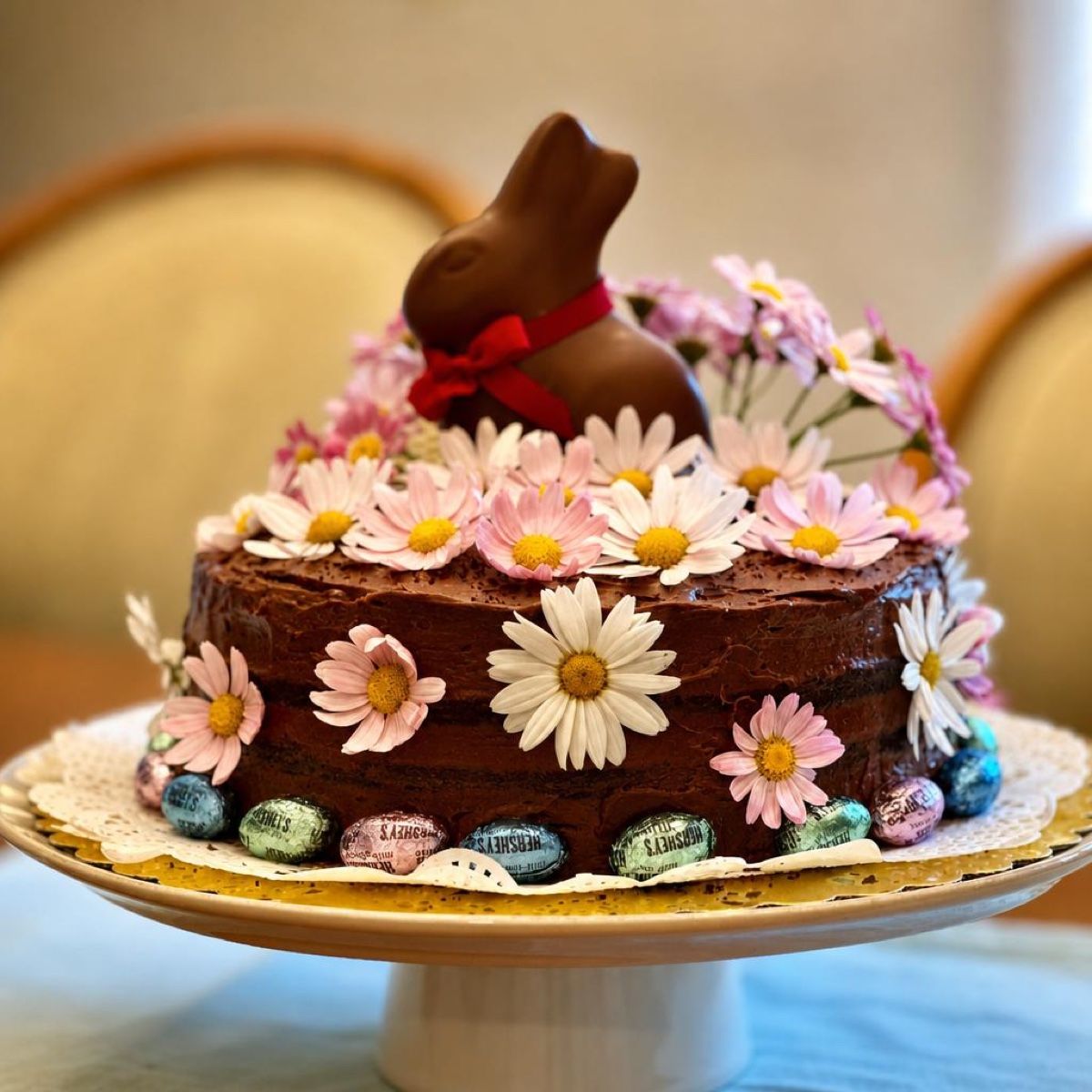 Chocolate Easter celebration cake topped with fresh daisies and a chocolate bunny, surrounded by mini foiled eggs — custom celebration cakes by Sienne's Table, Lomita CA