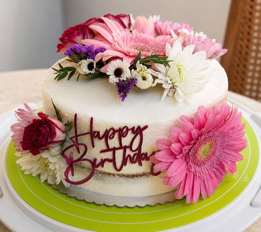 White celebration cake topped with pink gerbera daisies and fresh flowers — custom birthday cake by Sienne's Table, Lomita CA
