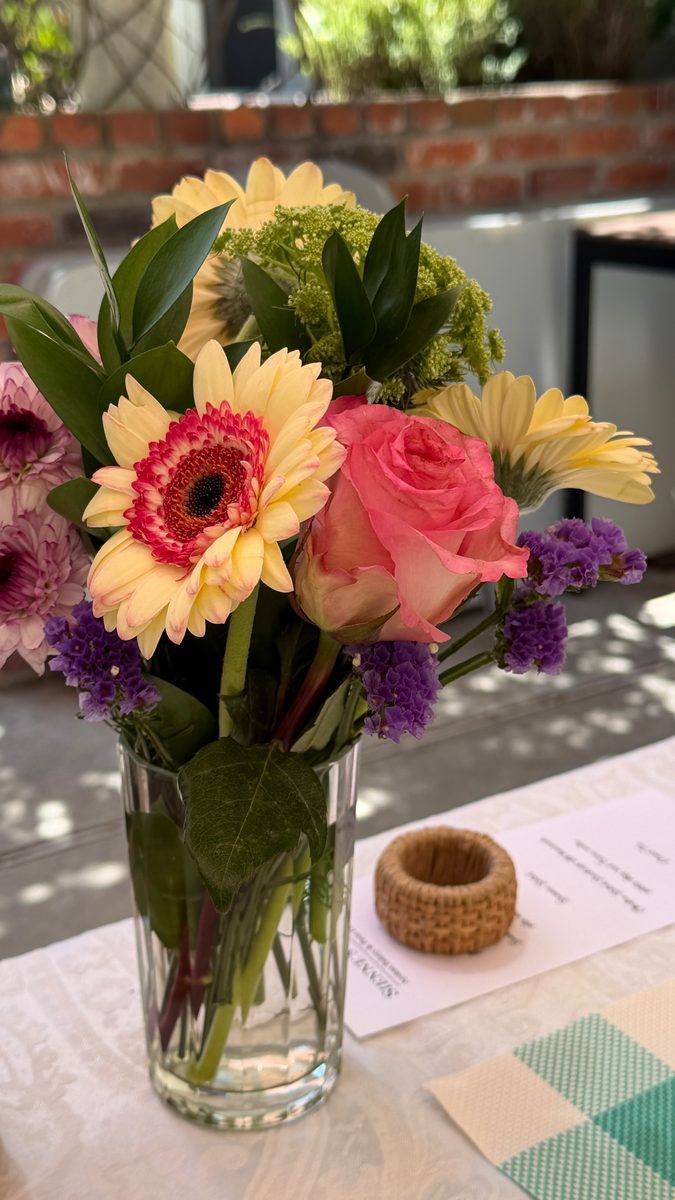 A jar of gerberas, roses, and statice on the lunch table beside a menu card