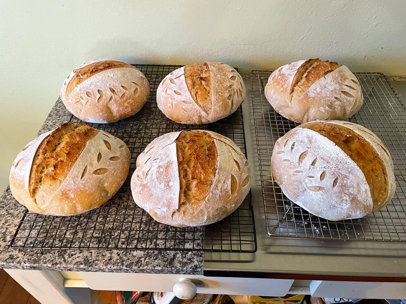 Six naturally leavened sourdough boules cooling on wire racks, scored with wheat-ear patterns — a single order from Sienne's Table
