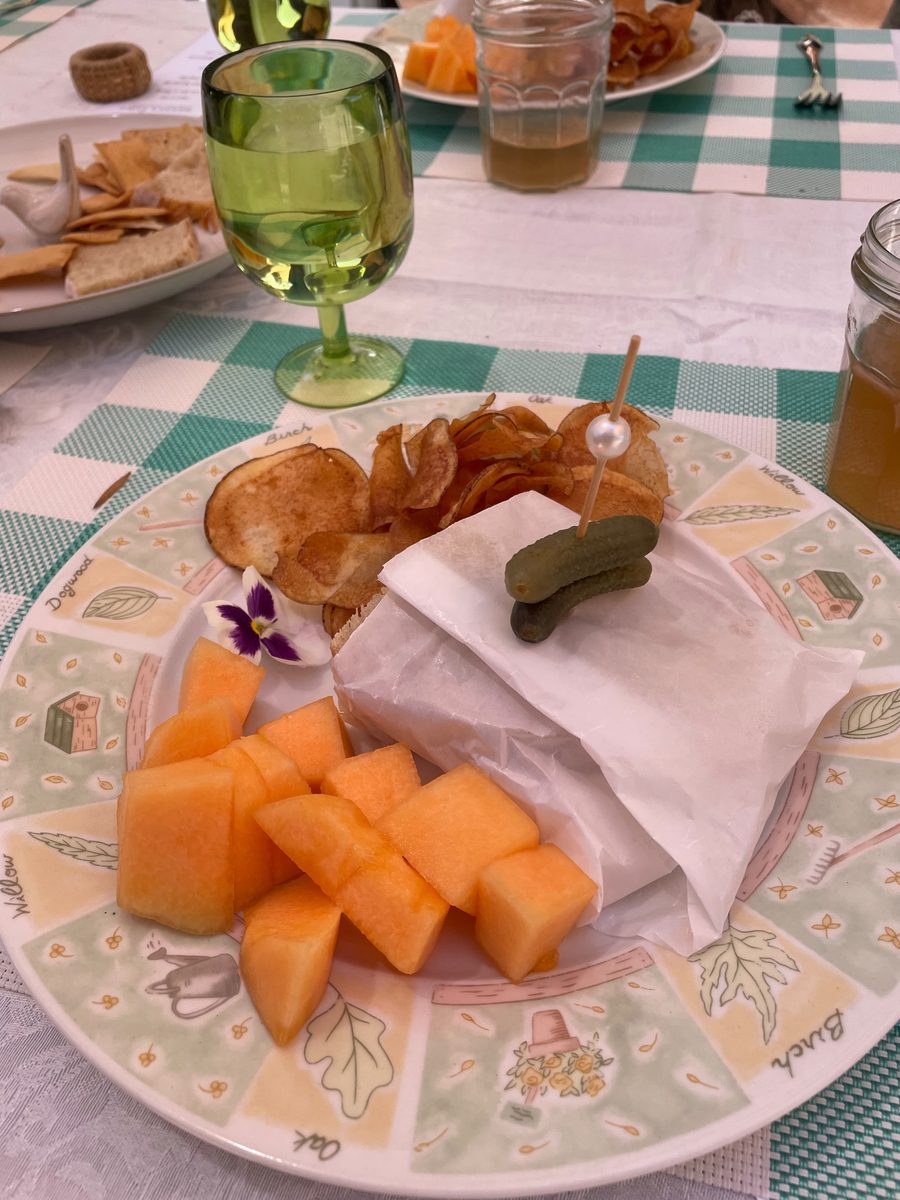 Chicken salad sandwich in paper with homemade potato chips, cornichons, and Tuscan melon — Patio Lunch at Sienne's Table