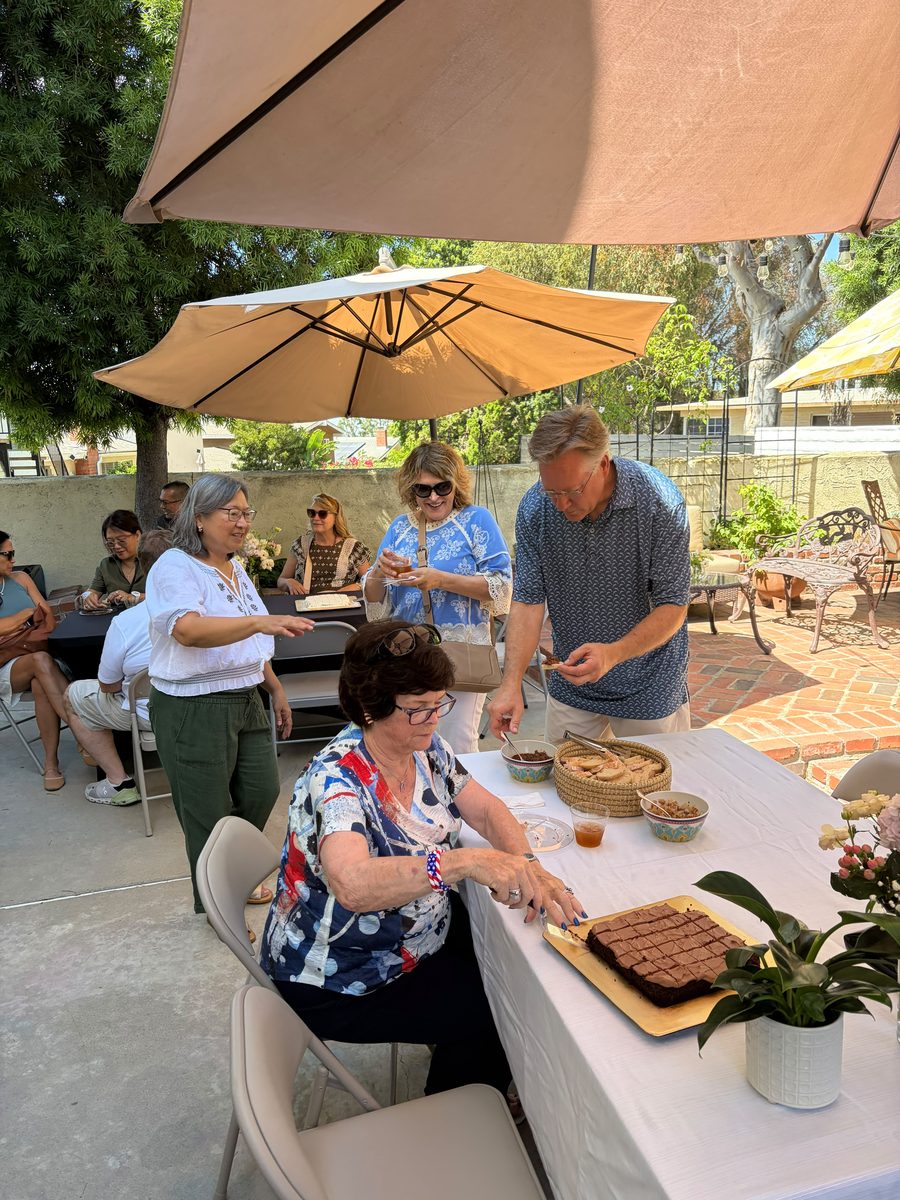 Guests gathered under patio umbrellas around a table of brownies and sourdough at the Sienne's Table Open House