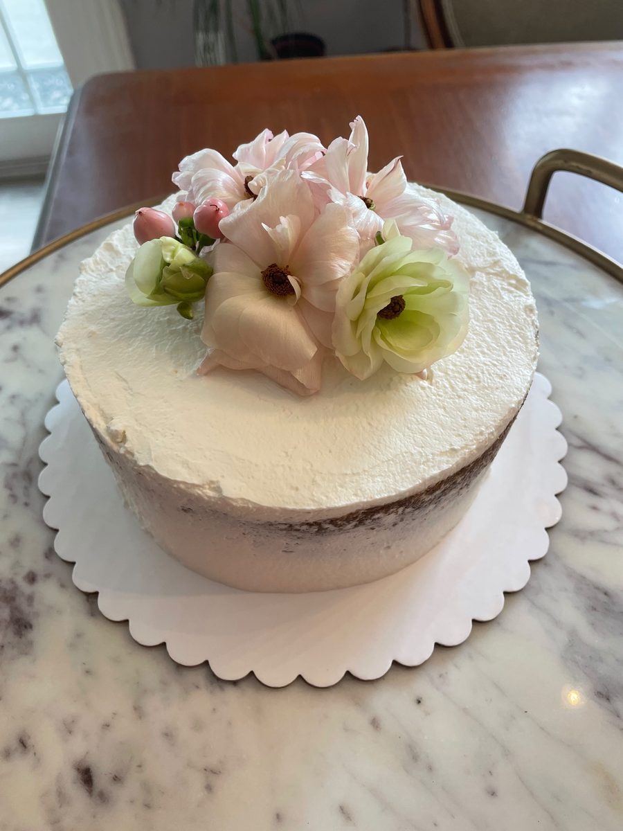 Naked layer cake crowned with pale pink ranunculus and green lisianthus on a marble stand — custom celebration cake by Sienne's Table