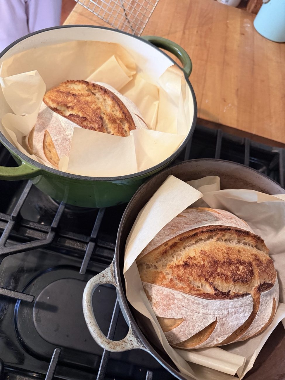 Two sourdough loaves in their Dutch ovens on the stovetop, just out of the oven
